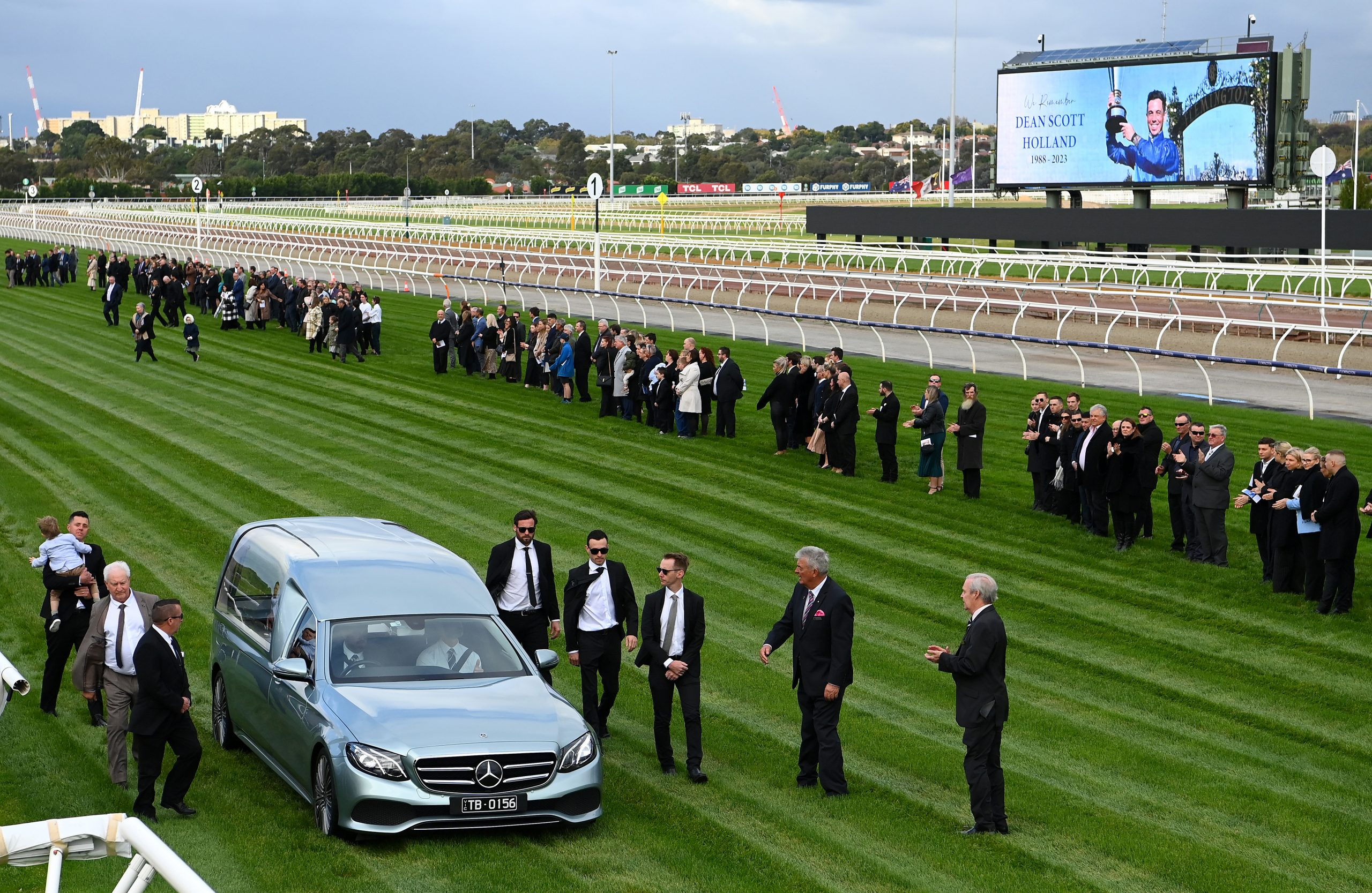 A guard of honour is formed as the hearse goes down the Flemington straight during a funeral service for jockey Dean Holland.
