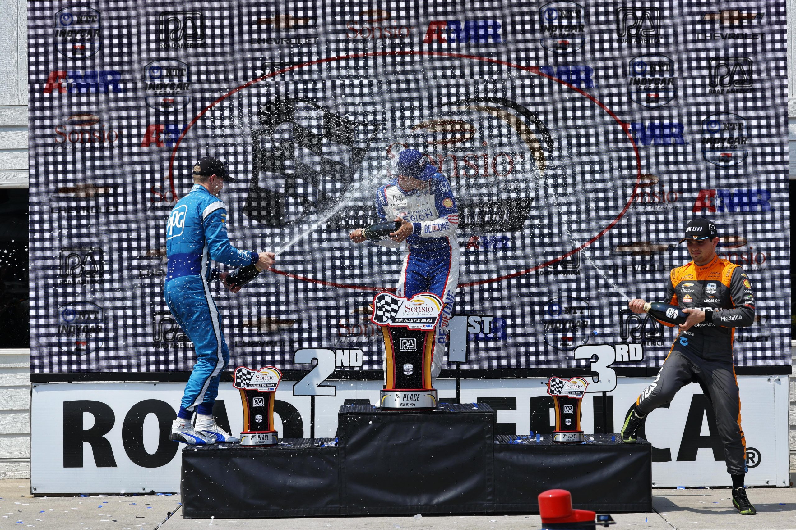 Josef Newgarden (left) celebrates on the podium with Alex Palou (centre) and Pato O'Ward (right).