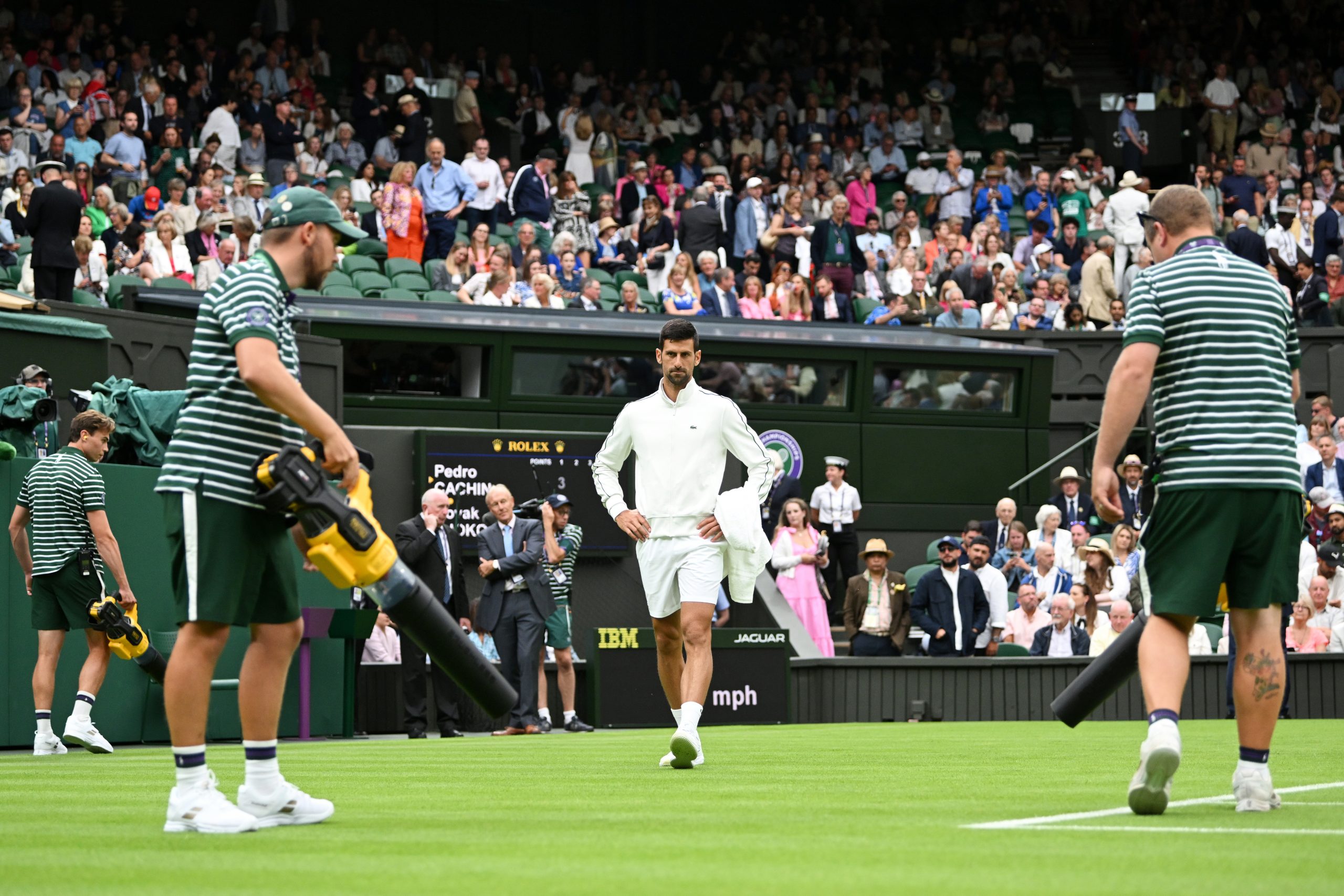 Novak Djokovic inspects the court as ground staff attempt to dry out the grass.