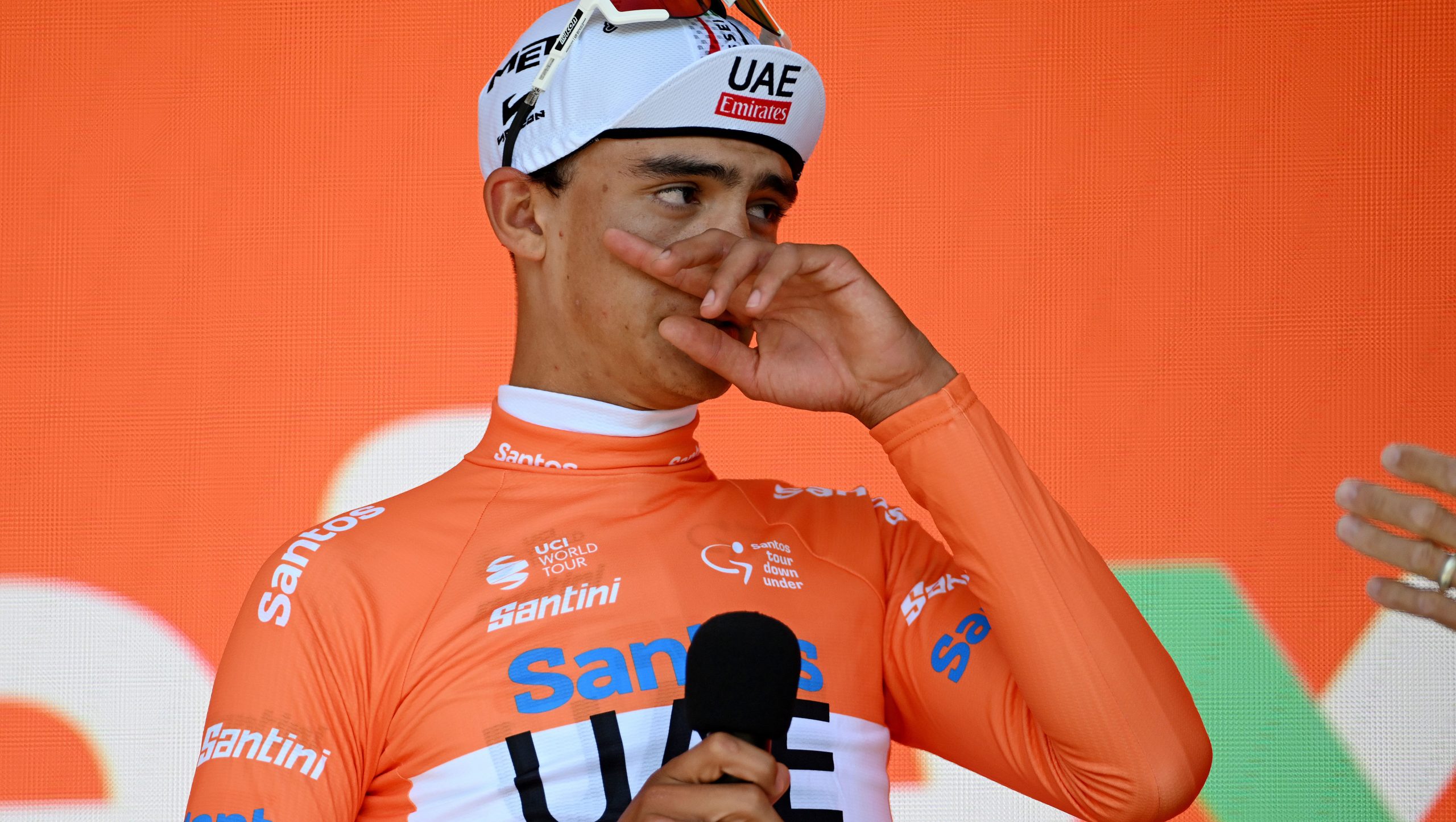 Isaac Del Toro Romero celebrates on the podium, wearing the orange leader's jersey.