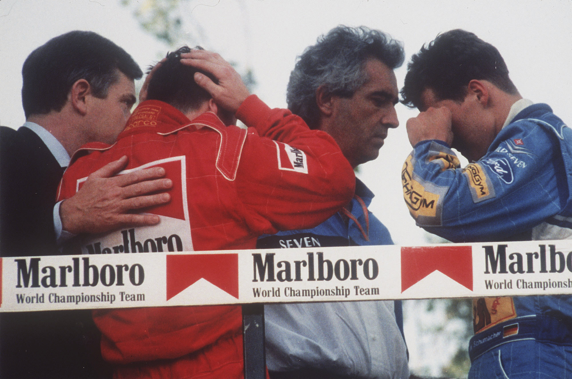 Italy's Nicola Larini, left, holds his head and Germany's Michael Schumacher, right, wipes a tear from his eyes while talking with Benetton director-general Flavio Briatore, center, on the podium following the San Marino Formula One Grand Prix crash in Imola, Italy, May 1, 1994. The drivers were reacting to the news that the Brazilian driver Ayrton Senna was in critical condition at a Bologna hospital.