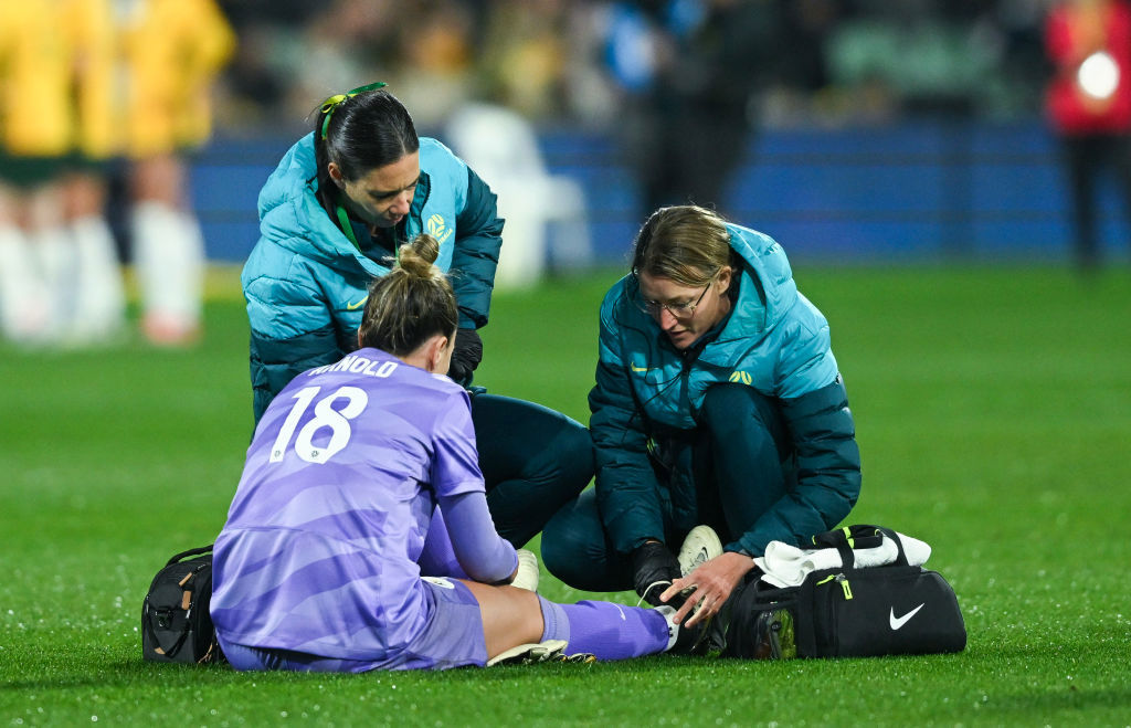 Mackenzie Arnold goalkeeper of Australia is helped by team medical staff.