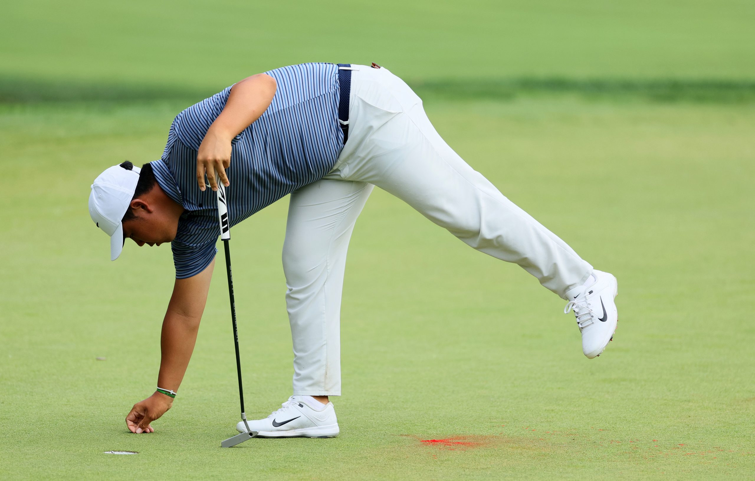 Tom Kim of South Korea prepares to putt on the 18th green while avoiding the red powder left by protesters.