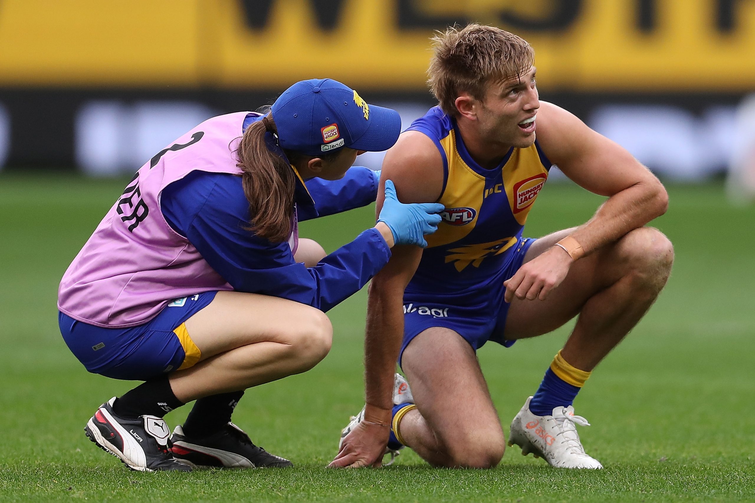 Brad Sheppard is attended to by a club trainer after a hit.