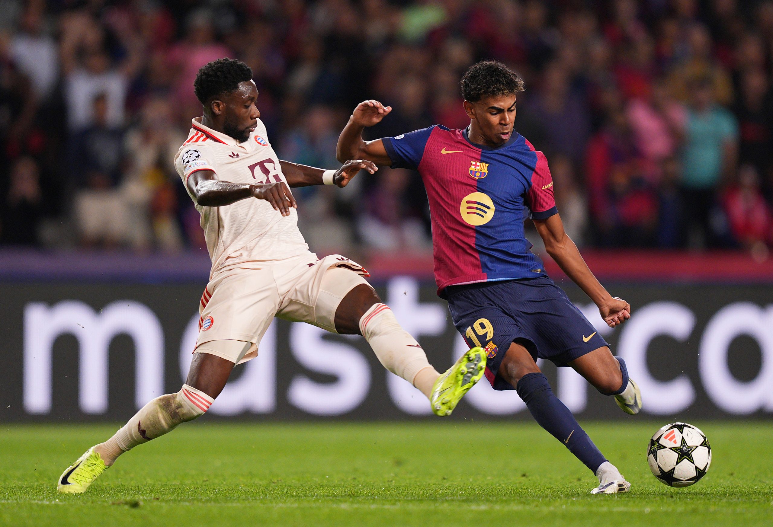 Lamine Yamal of Barcelona shoots under pressure from Alphonso Davies of Bayern Munich.