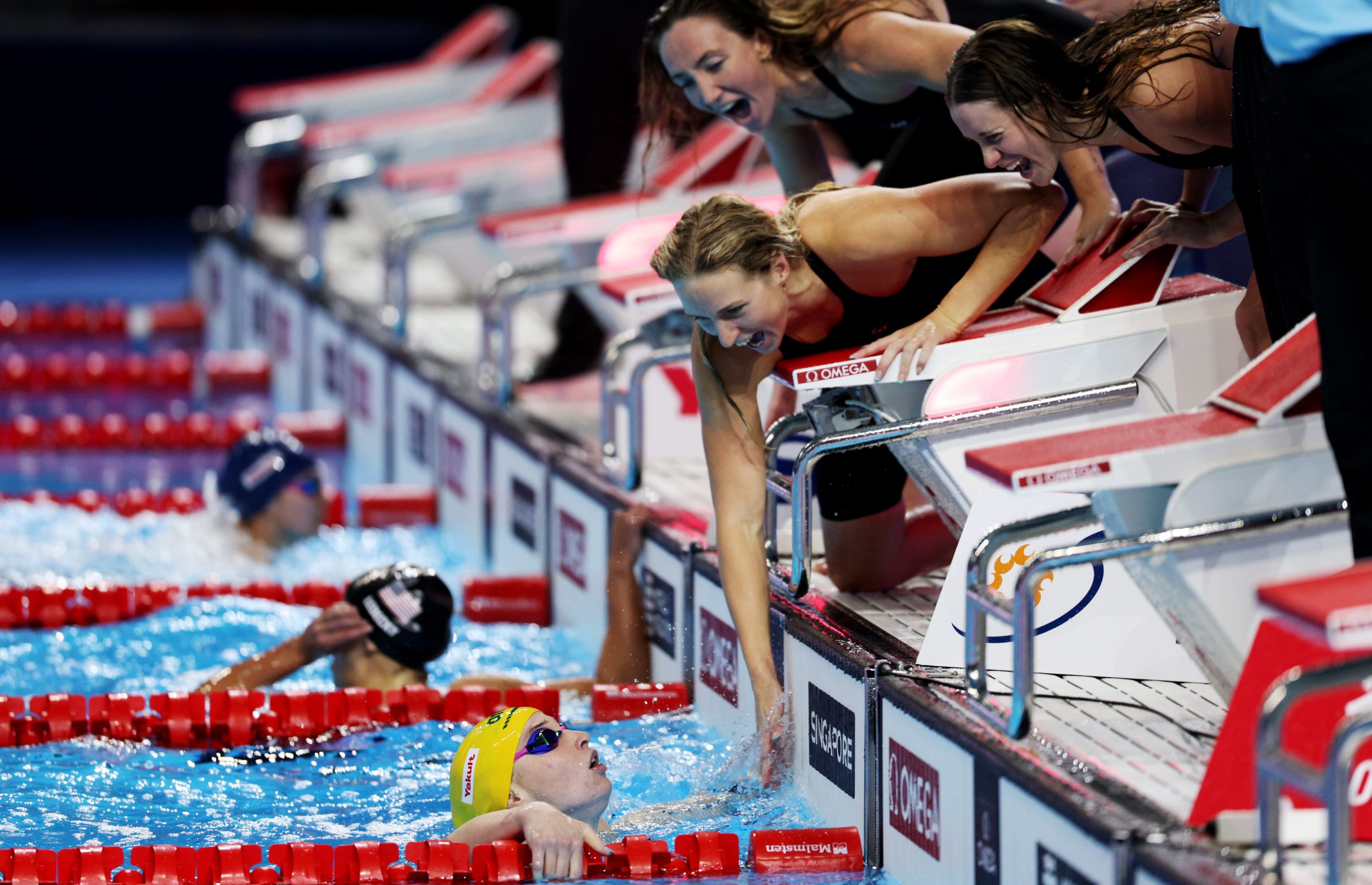 Mollie O'Callaghan is greeted by her relay teammates after completing the anchor leg.